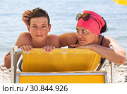 Mother pat her teenage son on the back while lying on yellow sun lounger on coastline, touching hair and looking at boy. Стоковое фото, фотограф Кекяляйнен Андрей / Фотобанк Лори