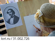 Женщина рисует портрет знаменитого французского артиста цирка Жан-Батиста Ориоля за мольбертом на бульваре в центре города Москвы в рамках уличного фестиваля "Москва - Париж", Россия (2019 год). Редакционное фото, фотограф Николай Винокуров / Фотобанк Лори