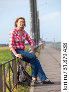 Mature woman hitchhiker sitting near road and waiting the car for ride. Стоковое фото, фотограф Кекяляйнен Андрей / Фотобанк Лори