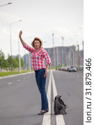 Middle age woman hail a taxi on road, stands on lane with backpack on asphalt. Стоковое фото, фотограф Кекяляйнен Андрей / Фотобанк Лори