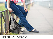 Unrecognizable female sitting on steel fence of pedestrian pathway with urban backpack on earth. Стоковое фото, фотограф Кекяляйнен Андрей / Фотобанк Лори