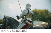 A man knight riding a horse around the battlefield and greeting the people watching behind the fence - raises his hand up in the sky holding a sword. Стоковое видео, видеограф Константин Шишкин / Фотобанк Лори