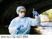 Female ecologist examines a test tube with water from a city river in a collector, holding a flask in her second hand. Стоковое фото, фотограф Евгений Харитонов / Фотобанк Лори