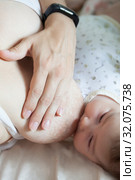 Baby breastfeeding, close-up view at infant head with female breast holding hand. Стоковое фото, фотограф Кекяляйнен Андрей / Фотобанк Лори
