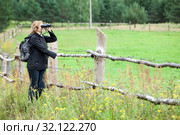 Backpack traveller standing in rural paddock with binocular, look through binoculars at distance, copyspace. Стоковое фото, фотограф Кекяляйнен Андрей / Фотобанк Лори