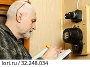 The man takes the readings of the apartment electric meter and writes it in the notebook. Стоковое фото, фотограф Акиньшин Владимир / Фотобанк Лори