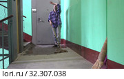 A young woman in blue jeans and a cage shirt swings and washes the floor on a staircase next to an elevator in a Stalinist-built apartment building, Cleaning public spaces by a labor immigrant cleane. Стоковое видео, видеограф Куликов Константин / Фотобанк Лори