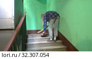 A young woman in blue jeans and a cage shirt swings and washes the floor on a staircase next to an elevator in a Stalinist-built apartment building, Cleaning public spaces by a labor immigrant cleane. Стоковое видео, видеограф Куликов Константин / Фотобанк Лори