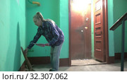 A young woman in blue jeans and a cage shirt swings and washes the floor on a staircase next to an elevator in a Stalinist-built apartment building, Cleaning public spaces by a labor immigrant cleane. Стоковое видео, видеограф Куликов Константин / Фотобанк Лори