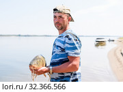 Только что пойманного большого сазана мужчина держит в руках на фоне реки (2019 год). Редакционное фото, фотограф Игорь Низов / Фотобанк Лори