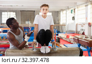 Male coach training teenage boy on gymnastic equipment at acrobatic hall. Стоковое фото, фотограф Яков Филимонов / Фотобанк Лори
