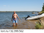 Только что пойманного сазана мужчина держит на кукане в воде на фоне реки солнечным днём (2019 год). Редакционное фото, фотограф Игорь Низов / Фотобанк Лори