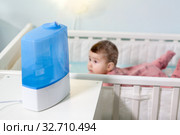Baby girl lying on stomach in crib with humidifier in use. Respiratory disease prevention at home. Стоковое фото, фотограф Кекяляйнен Андрей / Фотобанк Лори