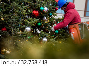 Рабочий вешает новогодние игрушки на елку, установленную на Манежной площади города Москвы, Россия (2019 год). Редакционное фото, фотограф Николай Винокуров / Фотобанк Лори
