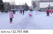 Дети катаются с ледяной горки на городской площади. Children ride on an ice slide in the town square. (2019 год). Редакционное видео, видеограф Евгений Романов / Фотобанк Лори