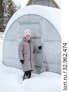 MAture Caucasian woman portrait standing knee-deep in snow near her snowcovered fiberglass greenhouse at winter season. Стоковое фото, фотограф Кекяляйнен Андрей / Фотобанк Лори