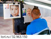 Tenerife, Spain - October 13, 2019: Back view male street painter make art using colorful pencils, artist draws from photography faces of children, photo taken in resort town of Los Cristianos, Spain. Редакционное фото, фотограф Alexander Tihonovs / Фотобанк Лори