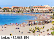 Tenerife, Spain - October 13, 2019: People sunbathing on sandy beach of Playa de los Cristianos, enjoy warm Atlantic Ocean waters, townscape and hotels exterior, Tenerife, Canary Islands, Spain. Редакционное фото, фотограф Alexander Tihonovs / Фотобанк Лори
