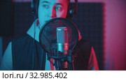 A man in hoodie rapping in the studio and recording his track wearing headphones. Стоковое видео, видеограф Константин Шишкин / Фотобанк Лори