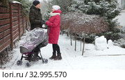 Young father and mother stand next to baby carriage, talking and holding hands on snowy yard of house, snowfall at winter season. Стоковое видео, видеограф Кекяляйнен Андрей / Фотобанк Лори