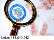 Эмблема Федеральной Налоговой службы Российской Федерации под лупой на фоне 5000 купюр. Стоковое фото, фотограф Николай Винокуров / Фотобанк Лори