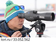 Coach of South Korea biathlon team watches biathletes in monocle at shooting range of biathlon arena. Junior biathlon competitions East of Cup (2019 год). Редакционное фото, фотограф А. А. Пирагис / Фотобанк Лори