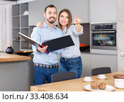Young beautiful couple standing with book in modern kitchen inte. Стоковое фото, фотограф Яков Филимонов / Фотобанк Лори