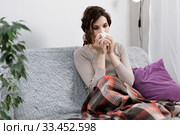 Sick woman suspected of covid-19, being at home in bed, measures the temperature and sneezes. Sick woman sitting under the blanket. Girl is quarantined with suspected coronavirus. Стоковое фото, фотограф Сергей Тимофеев / Фотобанк Лори