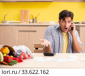 Young man calculating expences for vegetables in kitchen. Стоковое фото, фотограф Elnur / Фотобанк Лори