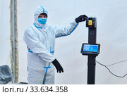 Medical officer invites to take non-contact temperature measurement in a tent of sanitary-epidemiological control in Perm, Russia (2020 год). Редакционное фото, фотограф Евгений Харитонов / Фотобанк Лори