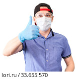 Portrait of delivery man gesturing wearing thumb up sign, wearing safety glasses, surgical mask and blue neoprene gloves, solated on white background. Стоковое фото, фотограф Кекяляйнен Андрей / Фотобанк Лори