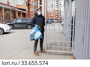 Adult Caucasian man wearing medical mask taking out the garbage to trash enclosure of residential house. Стоковое фото, фотограф Кекяляйнен Андрей / Фотобанк Лори