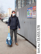 Adult man taking out garbage during coronavirus pandemic, it is allowed without any permission. Inscription on plate in Russian: trush enclosure and attention videosurveillance. Стоковое фото, фотограф Кекяляйнен Андрей / Фотобанк Лори