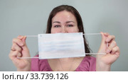 Close up view at medical mask in female hands, woman putting on one-use mask on face, grey background. Стоковое видео, видеограф Кекяляйнен Андрей / Фотобанк Лори
