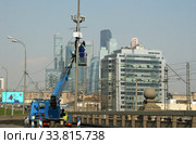 Рабочие на автовышке с телескопическим подъёмником. Наладка работы комплекса фотовидеофиксации нарушений ПДД. Москва, Новолужнецкий проезд, ТТК. Вид на «БЦ на Бережковской» и небоскребы Международного бизнес-центра "Москва-Сити" (2019 год). Редакционное фото, фотограф Щеголева Ольга / Фотобанк Лори