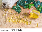 Прозрачные желатиновые овальные капсулы и флакон рыбьего жира на деревянном фоне. Омега-3 незаменимые полиненасыщенные жирные кислоты. Листья плюща и пеньковый шпагат. Стоковое фото, фотограф Наталья Гармашева / Фотобанк Лори