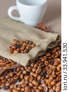 Roasted coffee beans, a white Cup, and a small burlap bag in close-up. Roasted coffee beans of the morning mood. Стоковое фото, фотограф Artem Sobov / Фотобанк Лори