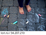 The child paints chalk on the path. Child draws patterns on asphalt. Square chalk of different sizes for drawing. Puffy legs of the baby and multicolored chalk. Стоковое фото, фотограф Александр Сергеевич / Фотобанк Лори