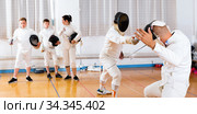 Coaches demonstrating to young athletes attack movements with rapier during fencing workout. Стоковое фото, фотограф Яков Филимонов / Фотобанк Лори