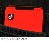 Приложение TikTok ("ТикТок") на экране мобильного телефона, лежащего в кармане джинсов (крупным планом) (2020 год). Редакционное фото, фотограф E. O. / Фотобанк Лори
