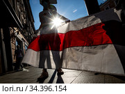 Мужчина держит бело-красно-белый государственный флаг Республики Беларусь в 1991—1995 годах у здания посольства Республики Беларусь на улице Маросейке в центре города Москвы, Россия (2020 год). Редакционное фото, фотограф Николай Винокуров / Фотобанк Лори