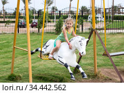 Little girl sitting on harseback of children swing, swinging on playground. Стоковое фото, фотограф Кекяляйнен Андрей / Фотобанк Лори