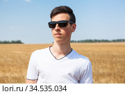 Teenage Caucasian boy portrait with black sunglasses, man stands on wheat field at sunny day, white t-shirt. Стоковое фото, фотограф Кекяляйнен Андрей / Фотобанк Лори