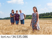 Concept of adopted kid, pretty girl standing on foreground with adoptive family on background, stepdaughter with dad, mom and preteen brother. Стоковое фото, фотограф Кекяляйнен Андрей / Фотобанк Лори