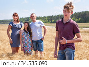 Concept of adopted child, boy standing on foreground with adoptive family on background, stepson with father, mother and pre-teen sister. Стоковое фото, фотограф Кекяляйнен Андрей / Фотобанк Лори