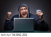 Young man wearing a hoodie sitting in front of a laptop computer. Стоковое фото, фотограф Elnur / Фотобанк Лори