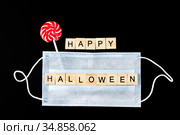 Striped colorful lollipop, medical mask and wooden words Happy Halloween on black. Halloween background decor holiday concept. Стоковое фото, фотограф Papoyan Irina / Фотобанк Лори