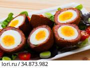 Tasty scotch eggs served with greens, leek and tomatoes at plate. Стоковое фото, фотограф Яков Филимонов / Фотобанк Лори