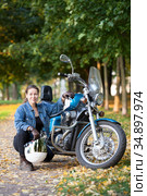 Biker woman with white helmet and jeans outfit portrait, sitting close to motorbike, autumn park. Стоковое фото, фотограф Кекяляйнен Андрей / Фотобанк Лори