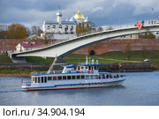 Прогулочный корабль "Садко" проходит под пешеходным мостом у кремля Великого Новгорода осенним днем (2020 год). Редакционное фото, фотограф Виктор Карасев / Фотобанк Лори
